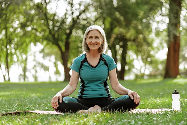 Older woman meditating under trees in a park
