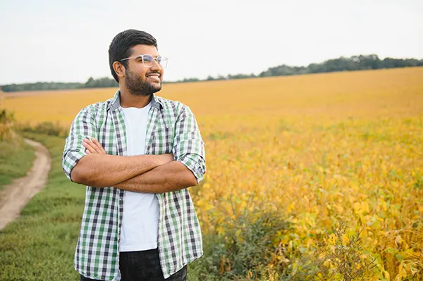 Man with glasses smiling with arms crossed looking into the distance at large grassy field